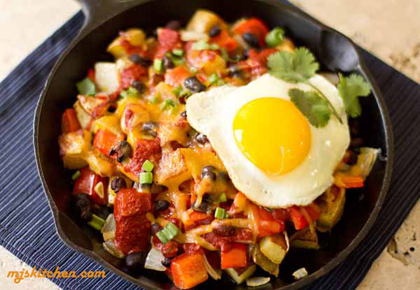 A skillet dish with potatoes, vegetables, chile, cheese and an egg